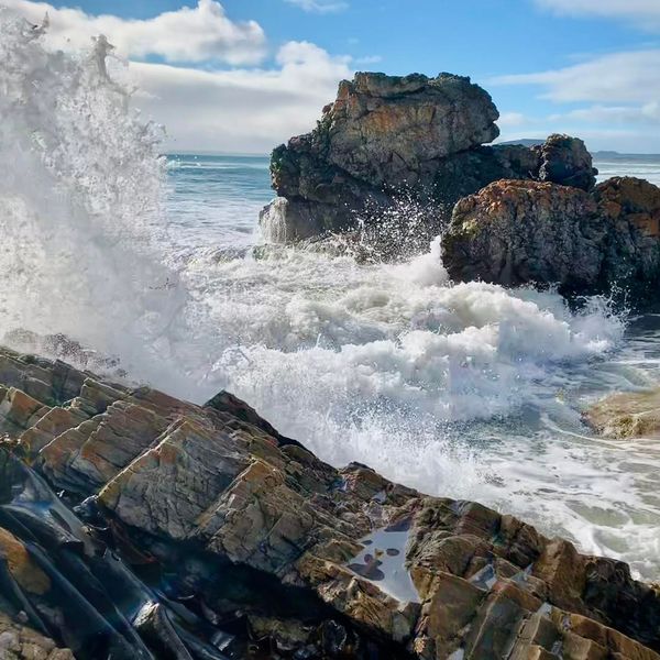 A wave breaking over coastal rocks under a blue sky