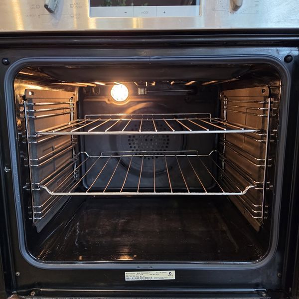 The inside of an oven after cleaning, with the light on and the racks back in